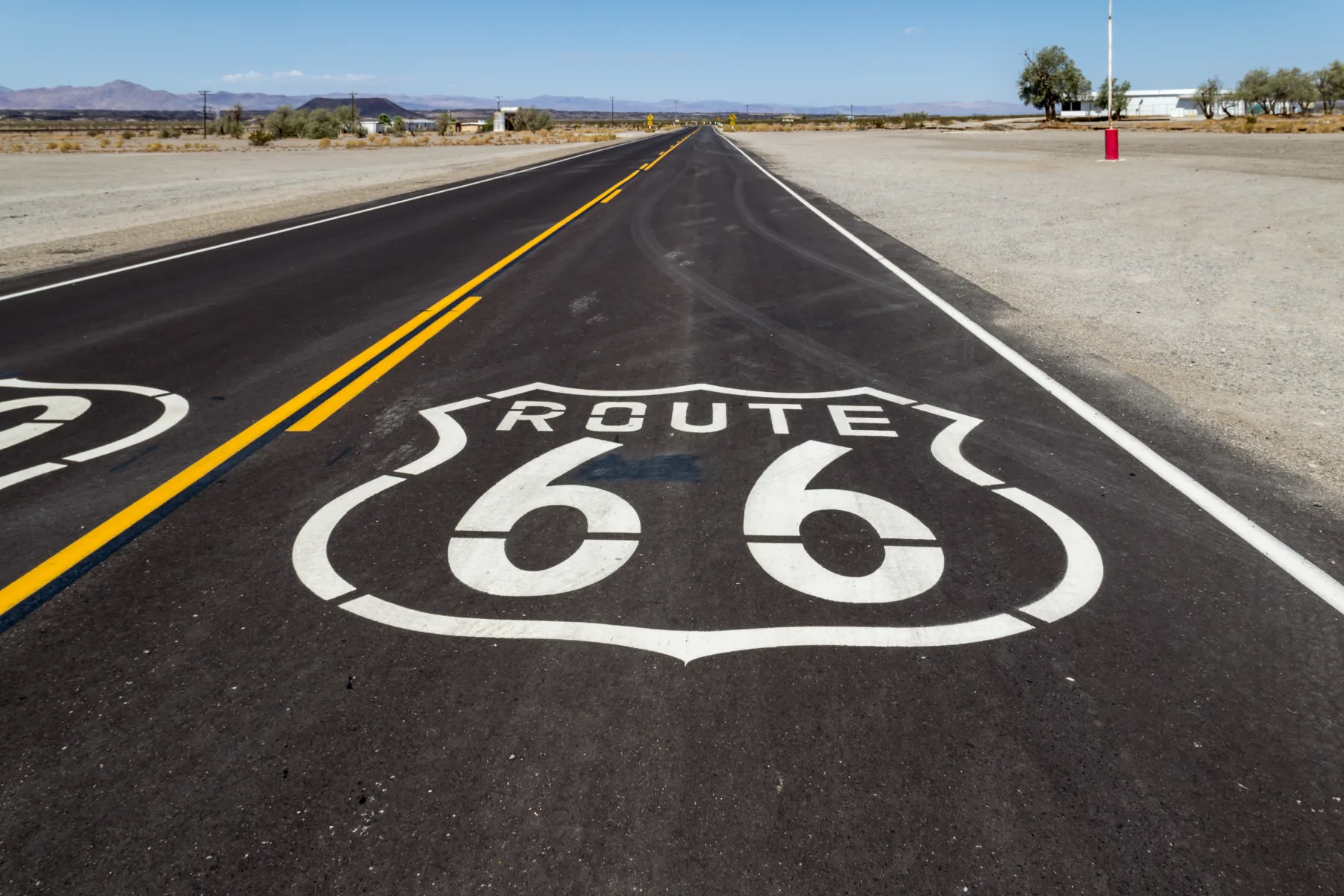 Escudos de la Ruta 66 pintados sobre el asfalto en una carretera recta de Amboy, California