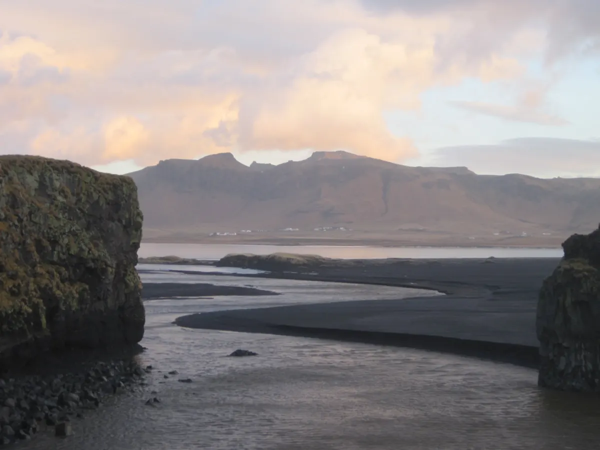 Río glaciar entre arena negra y montañas de Islandia