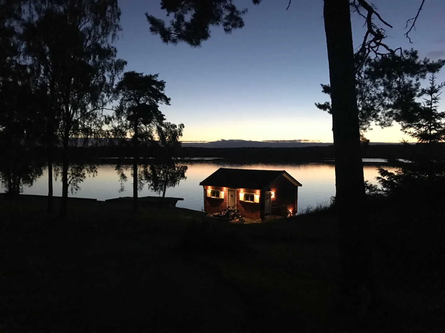 Cabaña de madera iluminada junto a un lago sueco al anochecer