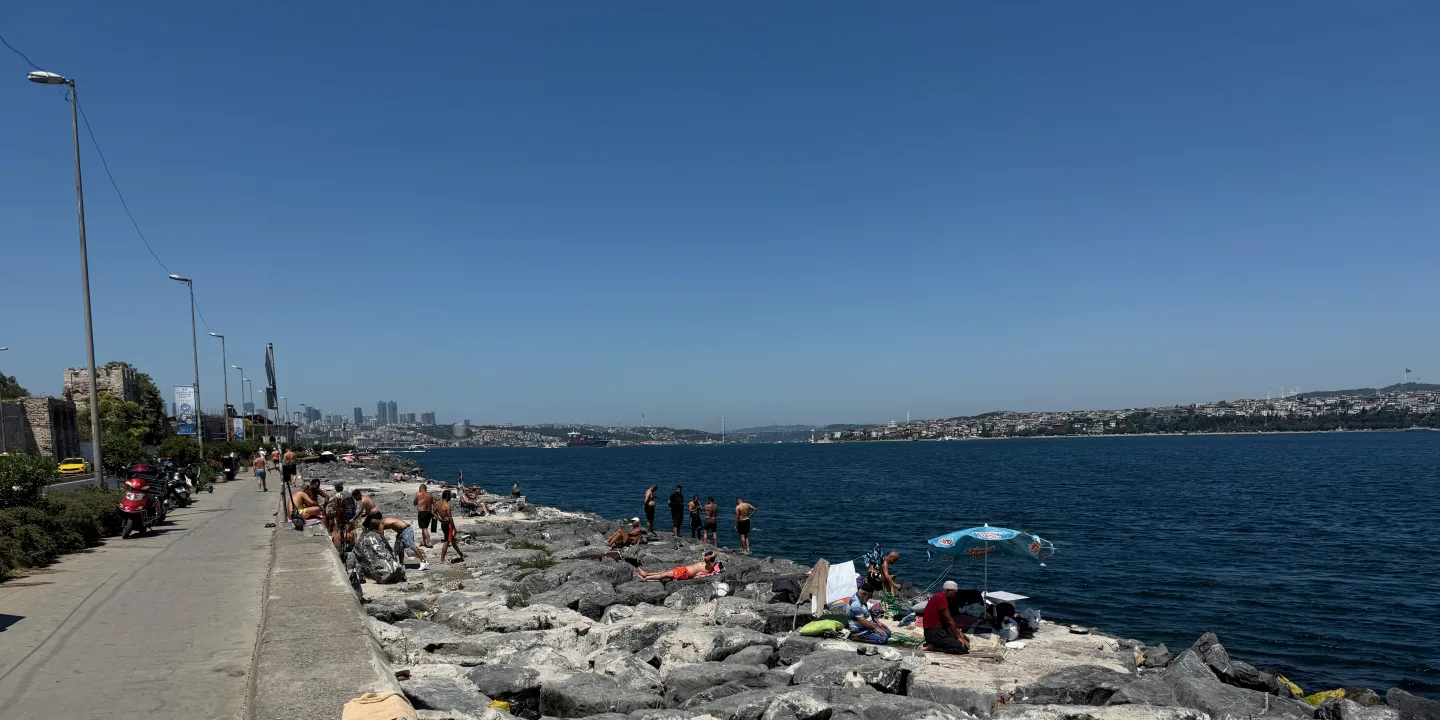 Orilla rocosa del Bósforo con bañistas y la ribera asiática de Estambul al fondo